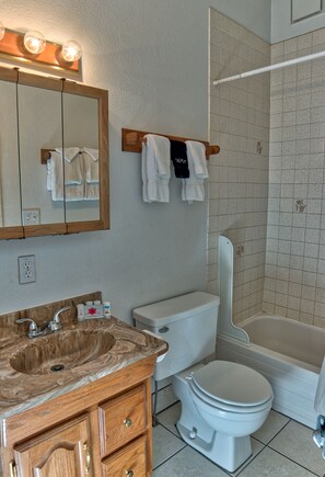 Une salle de bain avec un lavabo en marbre, des toilettes, une baignoire et un miroir surmonté de luminaires.