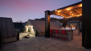 Eine Außenpatio-Terrasse mit Grillstation, roten Barhocker und Lichterketten.
