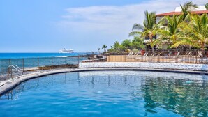 A pool with a curved edge, a metal fence, and a view of the ocean with a cruise ship in the distance. - 🏖️Garden View Kona Condo | A/C, Pools, Walk to Ocean (Kailua Kona)