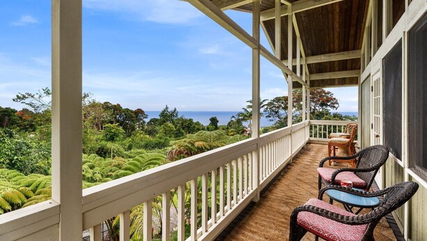 Een overdekt balkon met rieten meubilair, met uitzicht op een weelderig landschap en de oceaan.