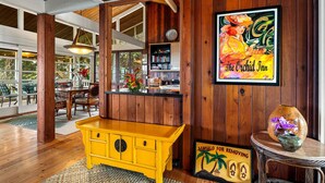 Een houten interieur met een geel aanrecht, een ingelijst kunstwerk en een bordje om schoenen uit te trekken.