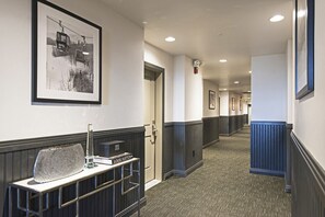 A hotel hallway with a framed picture of a ski lift, a reception desk with a Louis Vuitton box, and a blue radiator. - Main Street Condo|Steps to Lift |Amazing Rooftop I Managed by Park City Lodging (PARK CITY)