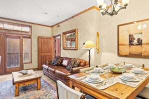 A dining area with a wooden table set for four, a brown leather sofa, and a chandelier. - Main Street Condo|Steps to Lift |Amazing Rooftop I Managed by Park City Lodging (PARK CITY)