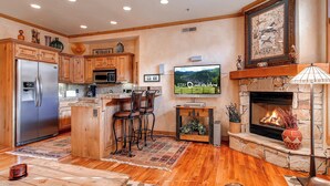 A modern kitchen with wooden cabinets, a stainless steel refrigerator, and a stone fireplace.