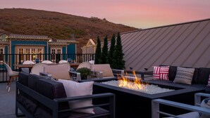 A rooftop patio with outdoor seating, a fire feature, and a view of a hillside.