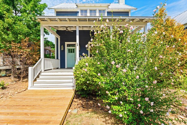 A two-story house with a porch, a front door, and a wooden deck leading to the entrance.