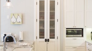 A kitchen with white cabinets, a double door with frosted glass panels, a microwave, and a pendant light. - Carlton Landing! Beautiful home with screened porch and outdoor fireplace! (Carlton Landing)