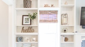 A living room with a white sofa, a bookshelf filled with books and decorative items, and a television on the wall. - Carlton Landing! Beautiful home with screened porch and outdoor fireplace! (Carlton Landing)