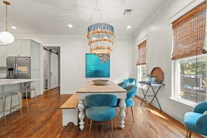 Een moderne keuken met een centraal eiland, een eethoek met blauwe stoelen, en een grote kroonluchter.