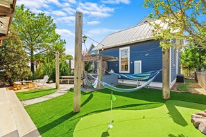 Een achtertuin met kunstgras, een hangmat, tuinmeubilair en een houten pergola.