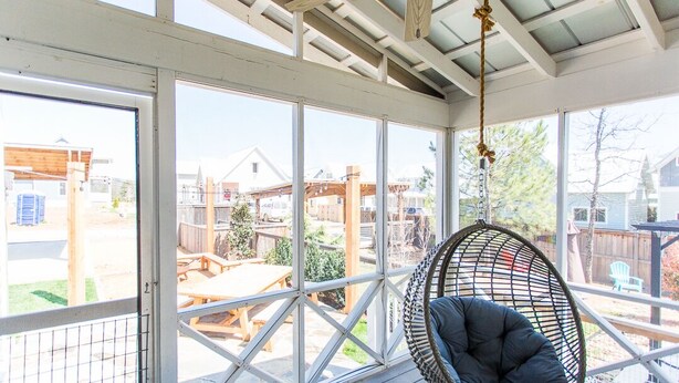 A covered outdoor area with a hanging chair, large windows, and a view of a backyard with a wooden deck and outdoor furniture. - Carlton Landing! Beautiful home with screened porch and outdoor fireplace! (Carlton Landing)