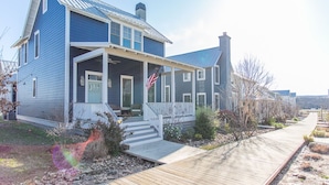 A two-story house with a porch, a front yard, and a wooden walkway. - Carlton Landing! Beautiful home with screened porch and outdoor fireplace! (Carlton Landing)