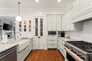 Een moderne keuken met witte kastjes, een houten vloer, een ingebouwde oven en een roestvrijstalen fornuis.