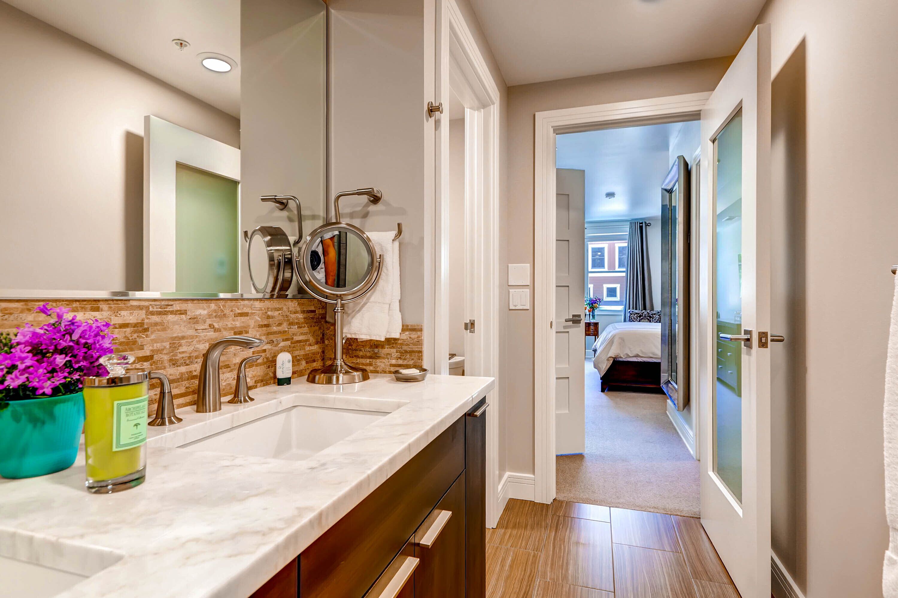 A modern bathroom with a large mirror, two sinks, and a potted plant.