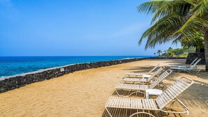 A beach with rows of wooden lounge chairs and a stone wall. - 🏖️Across from Oceanfront Pool | 1BR Kona Condo w/ AC (Kailua Kona)