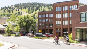 Vista de calle con un edificio de ladrillo, coches aparcados y ciclistas.