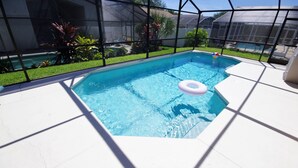 En rektangulär swimmingpool med en vit kant, omgiven av ett svart nätstaket, och en klarblå himmel i bakgrunden.