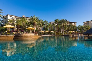 Una piscina cristallina con lettini e ombrelloni, circondata da palme e edifici.
