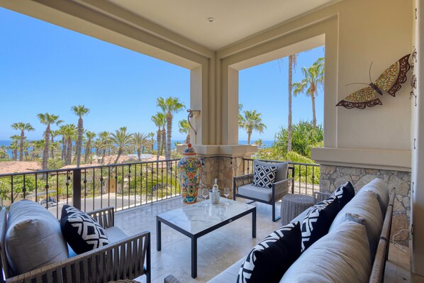 Un balcone con vista su palme e sull'oceano, arredato con un divano, sedie e un tavolo.
