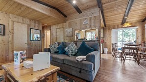 Un intérieur en bois avec un canapé gris, des coussins à motifs, une table basse en bois et un coin repas comprenant des chaises et une table en bois.