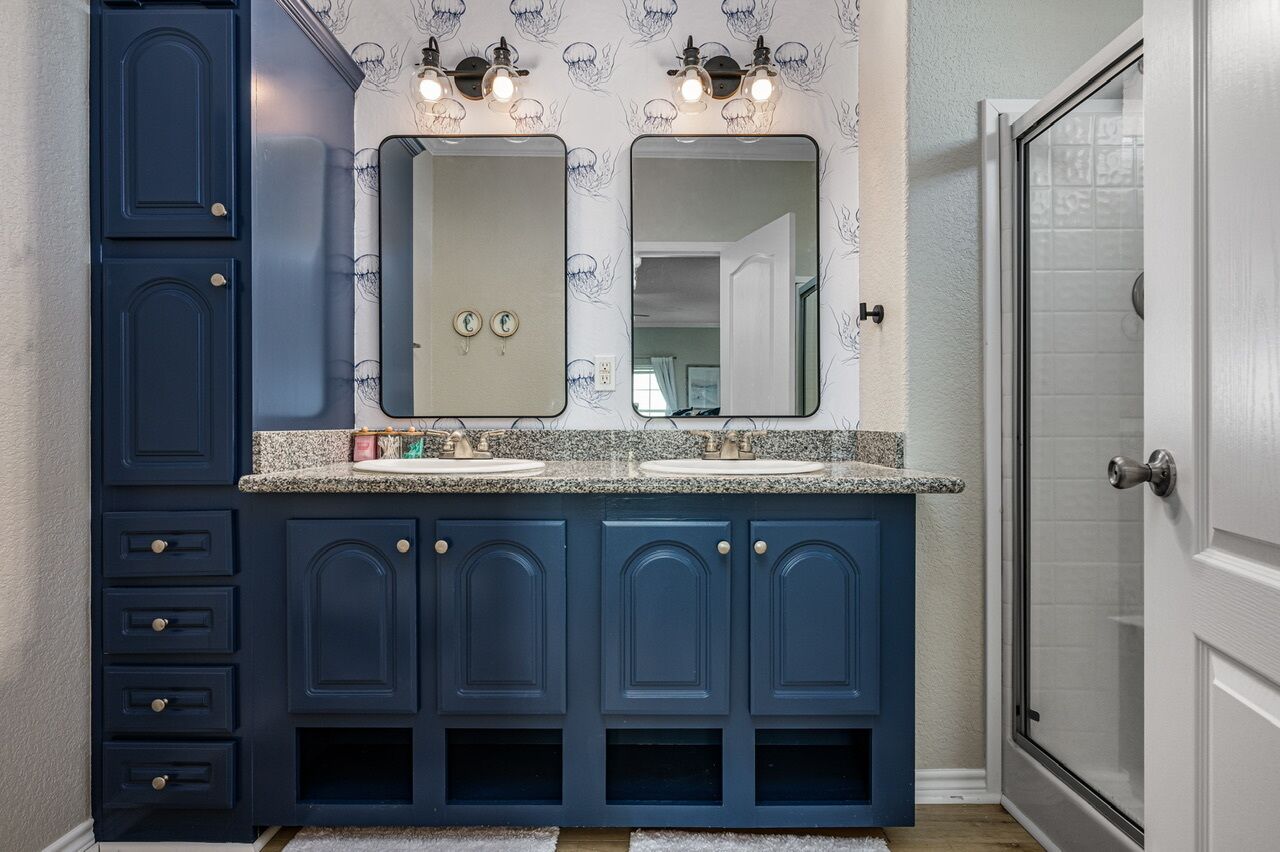 A bathroom with dark blue cabinets, two sinks, and a large mirror above the countertop.