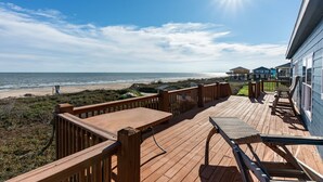 A wooden deck with lounge chairs overlooking a beach and ocean.