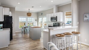 A modern kitchen with white cabinetry, a central island with stools, and a view of the outdoors.