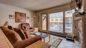 Un salon comprenant un canapé, un fauteuil et une table basse, un tableau accroché au mur et une fenêtre donnant sur des immeubles.