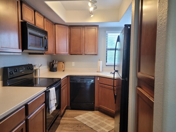 A compact kitchen with wooden cabinets, a black stove, a dishwasher, and a refrigerator. - Best of Tucson Views - Golf and Mountain in this personalized 2nd floor (Tucson)