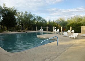 A swimming pool with a blue handrail, surrounded by white lounge chairs and trees. - Modern ranch house in East Tucson is set up for a perfect temporary stay (Tucson)
