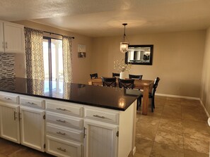 A kitchen with white cabinetry, a black countertop, and a dining area with a wooden table and chairs. - Modern ranch house in East Tucson is set up for a perfect temporary stay (Tucson)