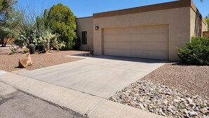 Une maison moderne de plain-pied avec un garage, entourée d’un jardin aménagé où l’on trouve différentes espèces de cactus et d’arbustes.