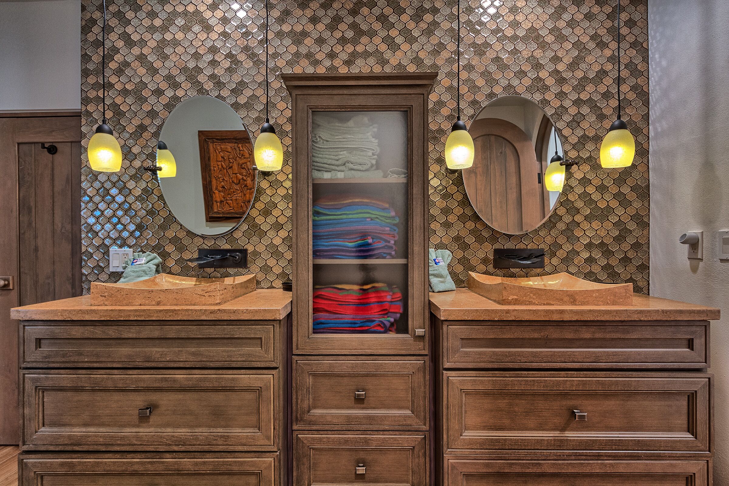 Un baño con dos lavamanos, armarios de madera y salpicadero de azulejos.