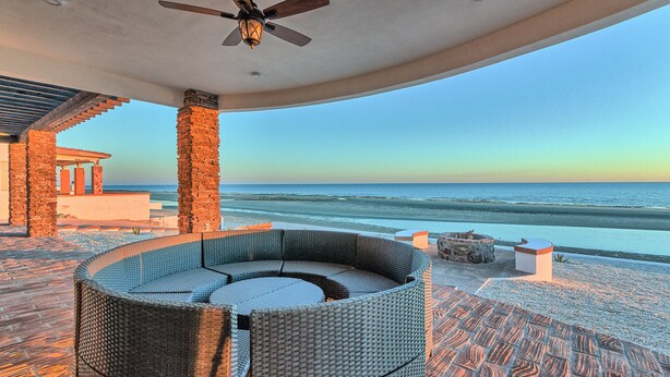 A circular wicker sofa with a ceiling fan, a stone pillar, and a view of the ocean.