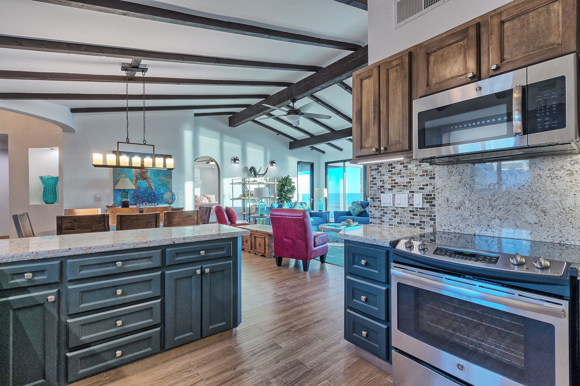 A modern kitchen with dark cabinetry, a large island, stainless steel appliances, and a view to the living area.