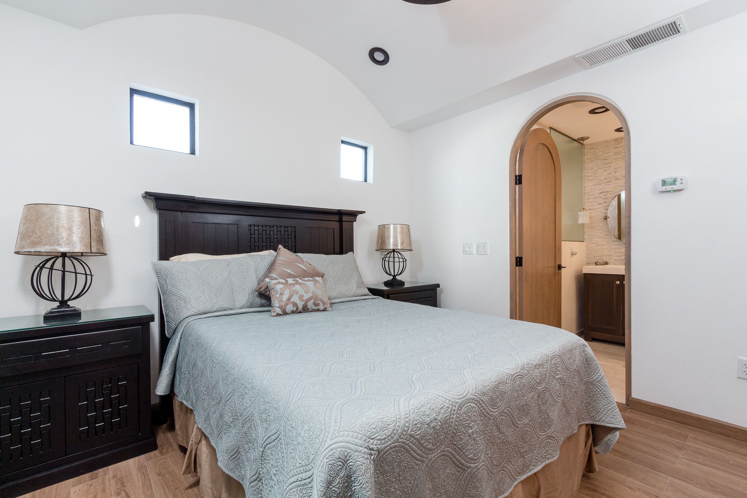A bedroom with a large bed, two bedside tables with lamps, a dark headboard, and a small window.
