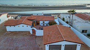 A coastal property with multiple buildings featuring red-tiled roofs and white walls, overlooking a beach and the sea.