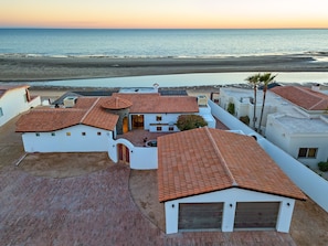 A coastal property with multiple buildings featuring red-tiled roofs and white walls, overlooking a beach and the sea.