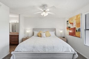 Une chambre à coucher avec un lit, des tables de chevet, un ventilateur de plafond, un miroir et un tableau accroché au mur.