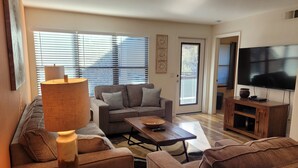 A living room with a sofa, coffee table, and TV stand. - Tucson flair in this 2nd floor-serene patio -close to main pool- exercise rm (Tucson)