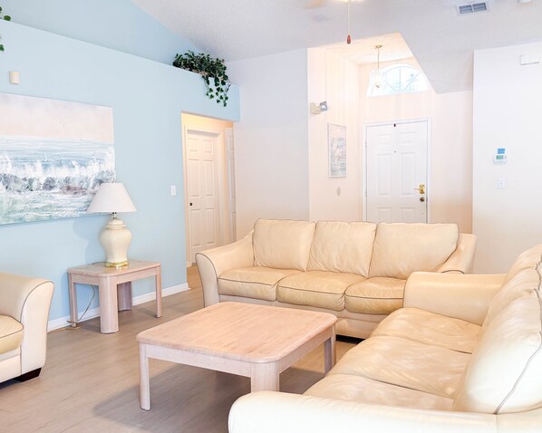 A living room with a beige sofa, a wooden coffee table, a lamp, and a painting on the wall. - Vacation Home with Private Pool Near Disney (Davenport)