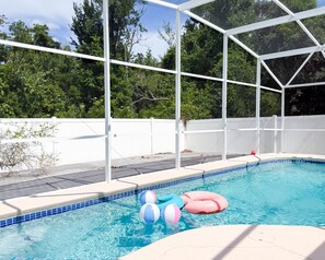 A swimming pool with a white fence, clear blue water, and inflatable pool toys. - Vacation Home with Private Pool Near Disney (Davenport)