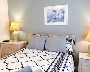 A neatly made bed with a patterned bedspread, two pillows, a framed picture on the wall, and two bedside lamps.