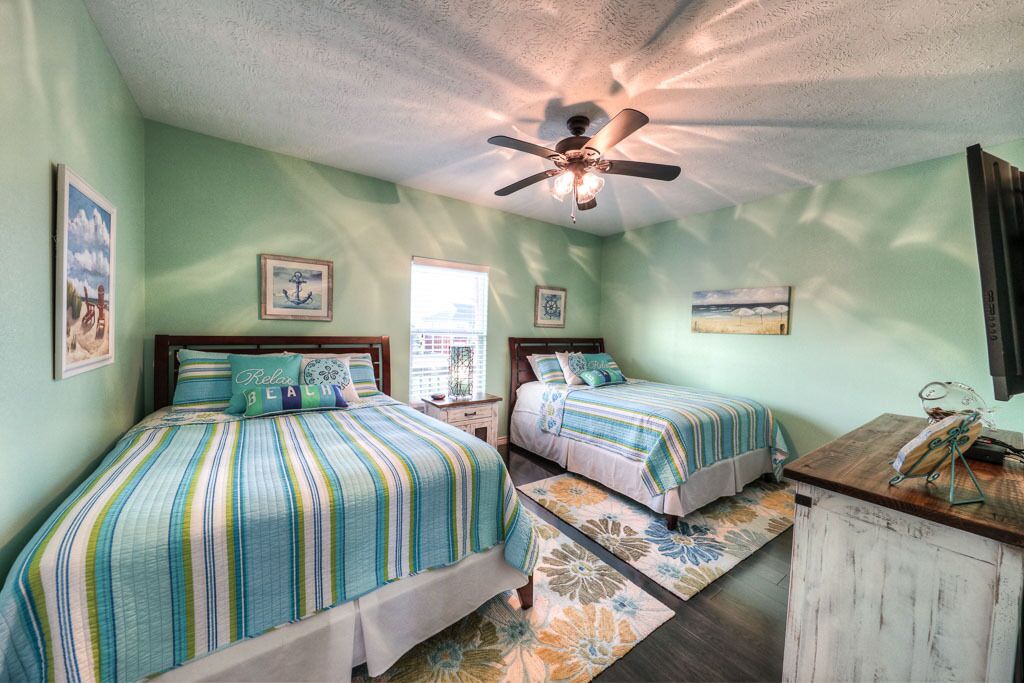 Une chambre avec deux lits, un ventilateur de plafond et des œuvres d’art accrochées aux murs.