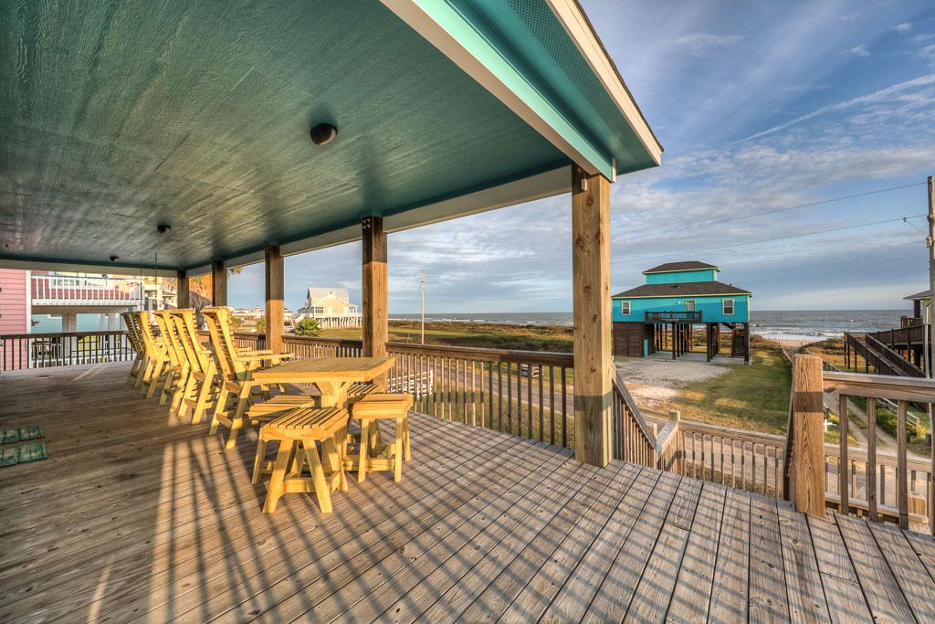 A wooden deck with outdoor furniture, a covered area, and a view of the beach and ocean.