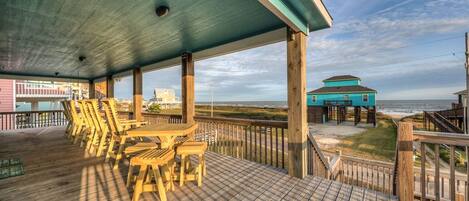 A wooden deck with outdoor furniture, a covered area, and a view of the beach and ocean.