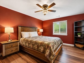 A bedroom with a wooden bed, two bedside tables, a ceiling fan, and a window with blinds.