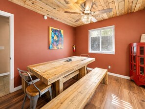 A dining area with a wooden table and benches, a ceiling fan, a window with blinds, and a red cabinet.