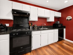 A kitchen with white cabinets, a black stove, and a red accent wall.