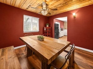 A dining area with a wooden table and chairs, a ceiling fan, and a window with blinds.